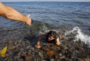 Yannis Behrakis - 17 september 2015 : Een lokale man helpt een Syrische vluchteling, die van boord sprong van een rubberboot, als hij uitgeput aankomt bij een strand op Lesbos